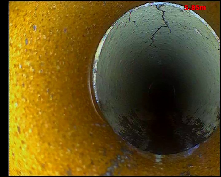 CCTV view through a pipe joint showing branching cracks running through the wall of the next pipe length