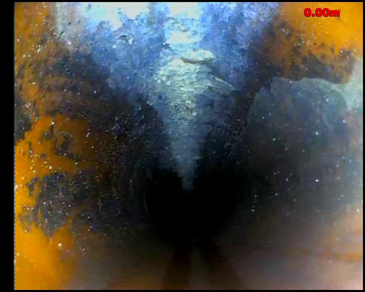 CCTV view inside a drain showing heavy orange and dark staining across the pipe wall